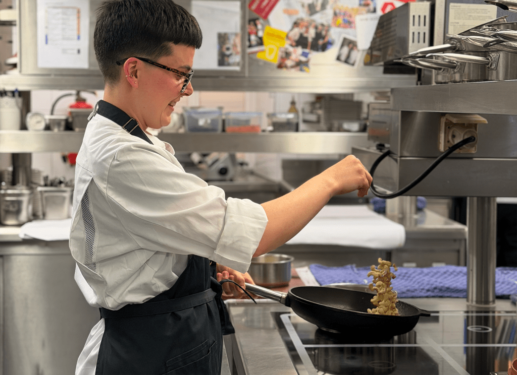 Köchin in Arbeitskleidung schwenkt Nüsse in einer Pfanne