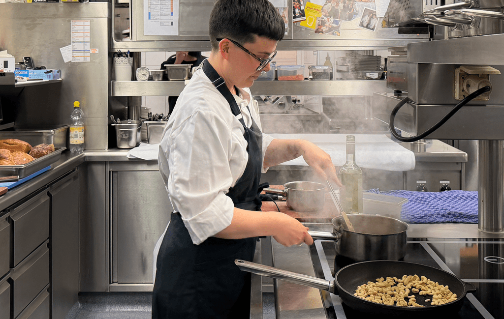 Junge Frau in Kochkleidung kocht in Küche mit eine Pfanne und einem Topf