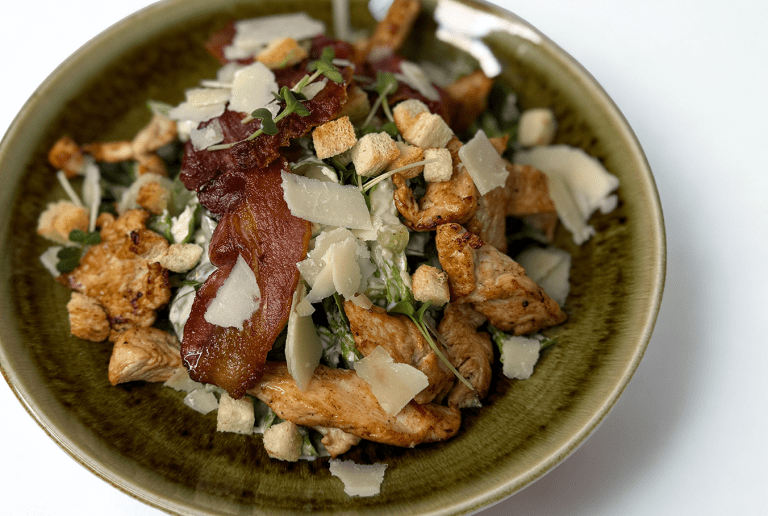 Nahaufnahme eines Tellers mit gebratenen Fleischstreifen, gemischt mit Brotcroutons, Parmesansplitter und Salat